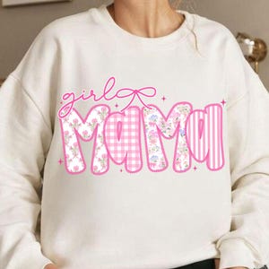 Puede incluir: Sudadera color crema con las palabras "girl mama" en rosa. La palabra "girl" est&aacute; en cursiva, y la palabra "mama" est&aacute; rellena de estampados florales, cuadros y rayas. Un lazo rosa est&aacute; encima de la palabra "girl".
