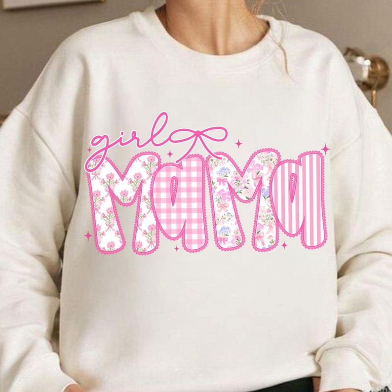 Puede incluir: Sudadera color crema con las palabras "girl mama" en rosa. La palabra "girl" est&aacute; en cursiva, y la palabra "mama" est&aacute; rellena de estampados florales, cuadros y rayas. Un lazo rosa est&aacute; encima de la palabra "girl".