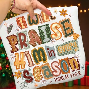 May include: White decorative pillow with the text "I WILL PRAISE HIM in every SEASON" in various colors and fonts. The pillow also includes the text "PSALM 146:2" and floral and leaf accents.