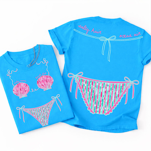 May include: Two turquoise t-shirts with beach-themed designs. One shirt features a seashell bra and bikini bottom graphic. The other shirt has a bikini bottom graphic and the words "salty hair, ocean air".