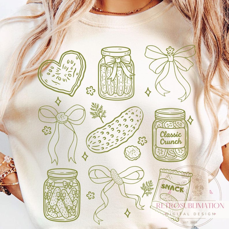 May include: Cream-colored t-shirt featuring a green line-art design of pickles, jars, bows, and a snack bag. The text "Classic Crunch" is on one jar. The design includes a heart-shaped pickle and the word "SNACK" on a bag.
