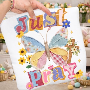 Può includere: Cuscino decorativo bianco con le parole "Just Pray" in lettere colorate. Il cuscino presenta una farfalla patchwork con accenti floreali e una croce, perfetto per la decorazione pasquale o primaverile.