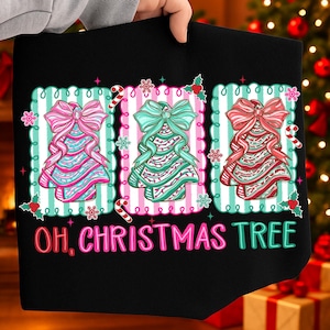 May include: Black t-shirt featuring three Christmas tree designs in pink, teal, and red, each with a bow and candy cane accents. The text "OH, CHRISTMAS TREE" is displayed in pink and green.