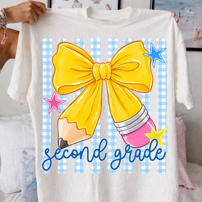 Może przedstawiać: Biały t-shirt z grafiką ż&oacute;łtej kokardy w kształcie oł&oacute;wka z r&oacute;żową gumką. Wz&oacute;r zawiera jasnoniebieskie tło w kratkę gingham, niebieskie, r&oacute;żowe i ż&oacute;łte gwiazdki oraz niebieski napis kursywą second grade.