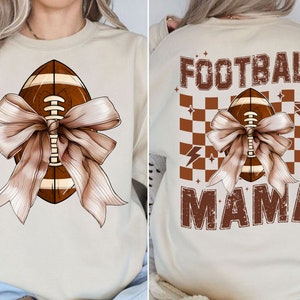 May include: A beige sweatshirt with a brown football tied with a brown bow. The text "FOOTBALL MAMA" is printed on the back of the sweatshirt with a brown checkered pattern.