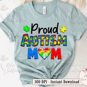 Pu&ograve; includere: Una maglietta blu chiaro con il testo "Proud Autism Mom" in nero, rosso e blu. Il testo &egrave; circondato da pezzi di puzzle di vari colori. Un pezzo di puzzle a forma di cuore &egrave; al centro del testo.