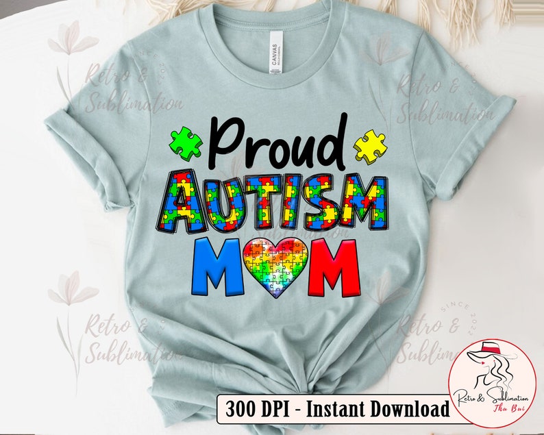 Pu&ograve; includere: Una maglietta blu chiaro con il testo "Proud Autism Mom" in nero, rosso e blu. Il testo &egrave; circondato da pezzi di puzzle di vari colori. Un pezzo di puzzle a forma di cuore &egrave; al centro del testo.