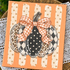 May include: A rectangular canvas print featuring a central pumpkin illustration with alternating segments of leopard print, black and white buffalo check, and black with white polka dots, topped with an orange and white gingham bow.
