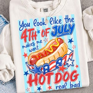 Puede incluir: Sudadera de color crema con un diseño gráfico que presenta un perrito caliente con temática patriótica. El texto dice "You look like the 4th of July makes me want HOT DOG real bad" en rojo y azul.