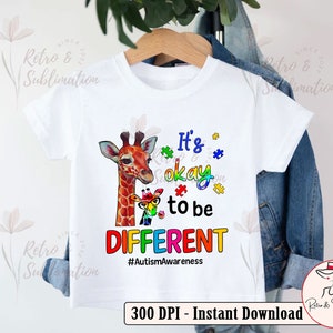 Pu&ograve; includere: Una maglietta bianca con un design di giraffa colorata e pezzi di puzzle. Il testo dice "It's okay to be DIFFERENT #AutismAwareness".