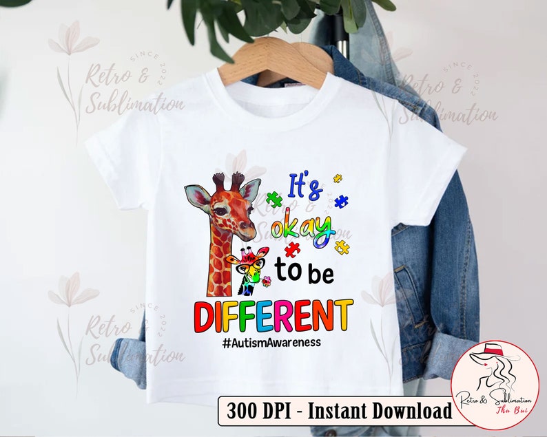 Pu&ograve; includere: Una maglietta bianca con un design di giraffa colorata e pezzi di puzzle. Il testo dice "It's okay to be DIFFERENT #AutismAwareness".