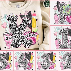 Könnte beinhalten: Cremefarbenes Sweatshirt mit einem großen "K"-Design für den Kindergarten, mit einem Apfel mit Discokugel, Bleistift und Becher. Zusätzliche Designs für die Vorschule bis zur 5. Klasse sind ebenfalls abgebildet.