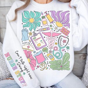 May include: White sweatshirt with a colorful graphic design of medical supplies and flowers. The text "Can't talk right now Doing NURSE STUFF" is printed on the sleeve.