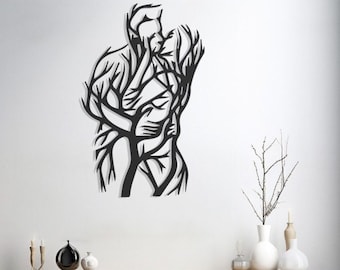 Puede incluir: Arte mural de metal negro que representa a una pareja abrazándose y besándose. Las figuras están estilizadas con un diseño de ramas de árbol, creando una representación artística única del amor y la conexión. La obra de arte está montada en una pared blanca.
