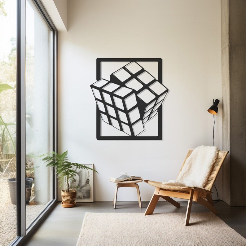 May include: Black and white Rubik's Cube wall art in a black frame. The cube appears to be partially emerging from the frame, creating a 3D effect. The artwork is displayed on a white wall in a modern living space.