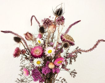 May include: A dried flower bouquet featuring pink, purple and white blooms. The bouquet includes dried thistle, daisies and other wildflowers.