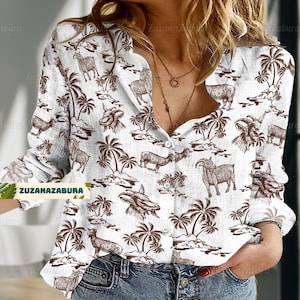 Könnte beinhalten: Ein weißes, langärmliges Hemd mit Knöpfen und einem braunen und weißen Druck von Palmen und Ziegen. Das Hemd hat eine lockere Passform und einen V-Ausschnitt.