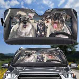 Op de afbeelding: Een zonnescherm voor auto's met vijf miniatuurschnauzers in een auto. De honden zijn allemaal grijs en zwart en zitten op de voor- en achterstoelen. Het zonnescherm is zwart en heeft een houtnerfpatroon.