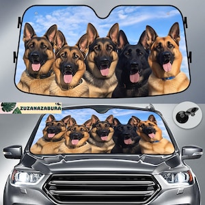 Op de afbeelding: Auto zonnescherm met een groep Duitse herdershonden tegen een blauwe lucht. De honden hebben bruine en zwarte vacht, met hun tong uit. De tekst "ZUZANAZABURA" is linksonder zichtbaar.