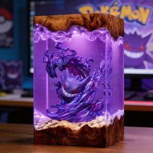 May include: A rectangular lamp featuring a purple Gengar figure encased in clear resin, surrounded by swirling purple smoke effects. The structure is framed by natural wood at the top and bottom, with internal lighting illuminating the purple resin.