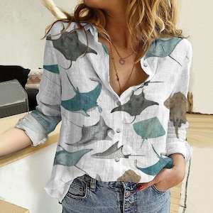 Könnte beinhalten: Weißes Button-Down-Shirt mit einem sich wiederholenden Muster aus stilisierten Mantarochen in Grau-, Türkis- und Brauntönen. Das langärmlige Hemd hat eine lockere Passform und ist aus leichtem Stoff gefertigt. Das Hemd ist oben aufgeknöpft.