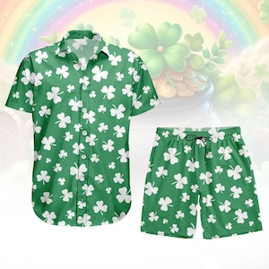 May include: A green shirt and shorts set, both patterned with white shamrocks. The short-sleeved shirt has a collar and buttons. The shorts have an elasticated waist with a drawstring. The background features a rainbow and a pot of gold, a St. Patrick's Day theme.