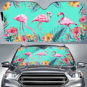 May include: A car sunshade featuring a vibrant design of pink flamingos, tropical flowers, and foliage against a teal background. The sunshade is designed to fit a car windshield and provides protection from the sun's rays.