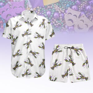 Peut inclure: Ensemble chemise et short blancs ornés d'un motif de crawfish verts, violets et jaunes. Le short est doté d'un cordon de serrage noir. En arrière-plan, des perles et des masques de Mardi Gras.