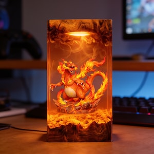 Könnte beinhalten: Eine rechteckige Kunstharzlampe mit einer orange-roten, drachenähnlichen Kreatur, die von geformten Flammen umgeben ist. Der Sockel und die Oberseite bestehen aus dunklem Holz, und das Innere leuchtet warm und beleuchtet die Kreatur und das Felsgelände.