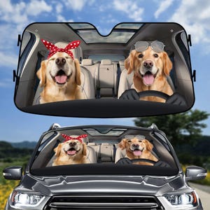 May include: A car sunshade with a photo of two golden retrievers. One dog is wearing a red and white polka dot headband and the other is wearing sunglasses. The sunshade is black and has a white border.
