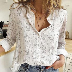Puede incluir: Camisa blanca de manga larga con botones y un estampado de pequeños conejos negros y corazones.