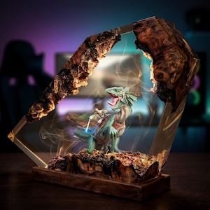 May include: A decorative lamp featuring a resin and wood frame enclosing a miniature scene of a figure riding a green lizard-like creature. The figure holds a glowing blue light sword, and wisps of smoke swirl around the central display.