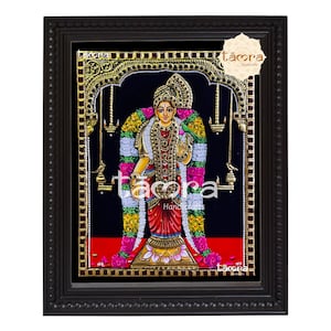 May include: A framed painting of a Hindu goddess with a golden halo and intricate floral decorations. The goddess is depicted in a standing pose with her hands in a prayer position. The painting is set against a black background and features a red border.