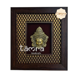 May include: A framed wall decor featuring a gold-coloured metal sculpture of a goddess with a crown and intricate details. The frame is brown wood with a gold and burgundy patterned background. The text "támra Handcrafts" is visible in the bottom right corner.