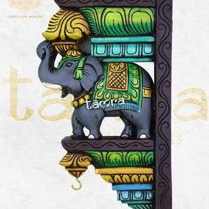 Puede incluir: Corbel de pared de elefante de madera pintado a mano con detalles coloridos. El corbel mide 30,5 cm de largo, 19 cm de ancho y 3,8 cm de profundidad. Presenta un elefante gris con un paño estampado amarillo y verde drapeado sobre su espalda. El corbel es un elemento decorativo utilizado en arquitectura y diseño.