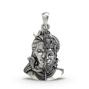 May include: A silver pendant featuring a split design with two faces. One side depicts a serene figure with a cobra, the other a detailed, ornate face. The pendant has a loop for a chain.