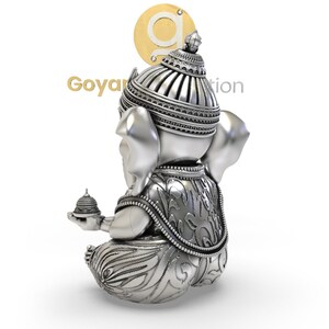 May include: A silver-colored statue of the Hindu deity Ganesha, seated with intricate details. The statue features a detailed headdress, ornate clothing, and a small offering in one hand. The image includes the text "Goyan Creation".