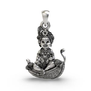 Può includere: Un ciondolo d'argento raffigurante una scultura dettagliata di una figura seduta adornata da una corona e gioielli. La figura è seduta in una barca decorativa con motivi ornati. Il ciondolo ha un anello per una catena.