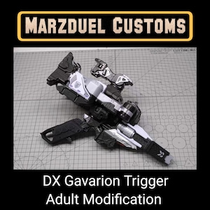 Puede incluir: Una pistola de juguete negra, blanca y plateada, la DX Gavarion Trigger, se muestra sobre una esterilla de corte gris. El texto "Marzduel Customs" está en un rectángulo negro con borde dorado en la parte superior. Debajo, el texto dice "DX Gavarion Trigger Adult Modification".