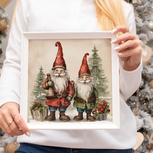 K&ouml;nnte beinhalten: Ein wei&szlig; gerahmter Druck mit zwei Gnomen, die in einer verschneiten Waldlandschaft stehen. Die Gnomen tragen rote und gr&uuml;ne H&uuml;te und haben wei&szlig;e B&auml;rte. Der Druck hat einen Vintage-Aquarellstil.