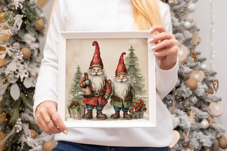 K&ouml;nnte beinhalten: Ein wei&szlig; gerahmter Druck mit zwei Gnomen, die in einer verschneiten Waldlandschaft stehen. Die Gnomen tragen rote und gr&uuml;ne H&uuml;te und haben wei&szlig;e B&auml;rte. Der Druck hat einen Vintage-Aquarellstil.