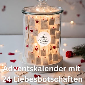 Könnte beinhalten: Ein Glasbehälter mit Deckel, gefüllt mit kleinen Notizen und roten Herzdekorationen, beleuchtet von Lichterketten. Der Behälter hat einen weißen Sockel und einen runden Aufkleber mit Text. Am unteren Rand steht "Adventskalender mit 24 Liebesbotschaften".