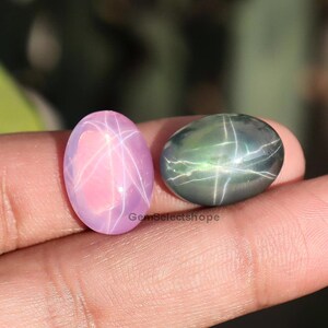 May include: Two oval gemstones, one pink with a star effect and the other dark green with a similar star pattern. The gemstones are held in a hand, with the text "GemSelectshope" visible.