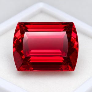 May include: A vibrant, rectangular-cut red gemstone with sharp, clean facets that create a brilliant, reflective surface. The stone displays a deep, saturated crimson hue throughout its structure, showcasing precise geometric symmetry and clarity.