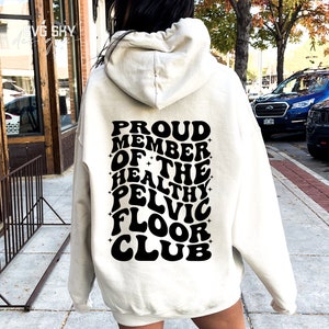 May include: A white hoodie with a black graphic that says "Proud Member of the Healthy Pelvic Floor Club" in a retro font.