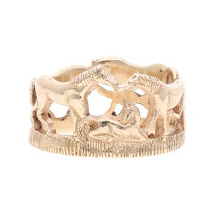 Puede incluir: Un anillo dorado con un diseño de carrusel de caballos. El anillo tiene una base texturizada y una serie de caballos en una disposición circular. Los caballos están esculpidos con un estilo detallado y tridimensional.