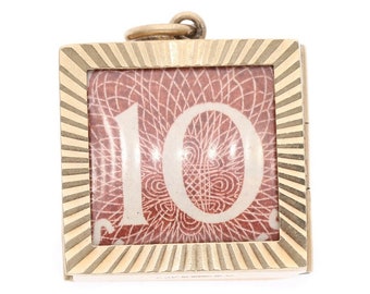 Può includere: Ciondolo pendente dorato con una cornice quadrata con un designo rosso e bianco e il numero "10" al centro.