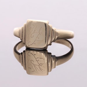 Può includere: Un anello a sigillo in oro con una faccia quadrata che presenta una lettera "F" incisa.