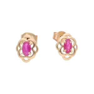 May include: A pair of stud earrings featuring oval-cut vibrant pink gemstones set in a gold-toned metal frame. The setting has a decorative, openwork floral or clover-like shape surrounding each central stone, secured with a post-back closure.