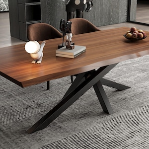 May include: A modern dining table with a dark wood top and a black metal base. The table is surrounded by brown chairs and sits on a gray rug. A decorative lamp and a bowl of fruit are on the table.